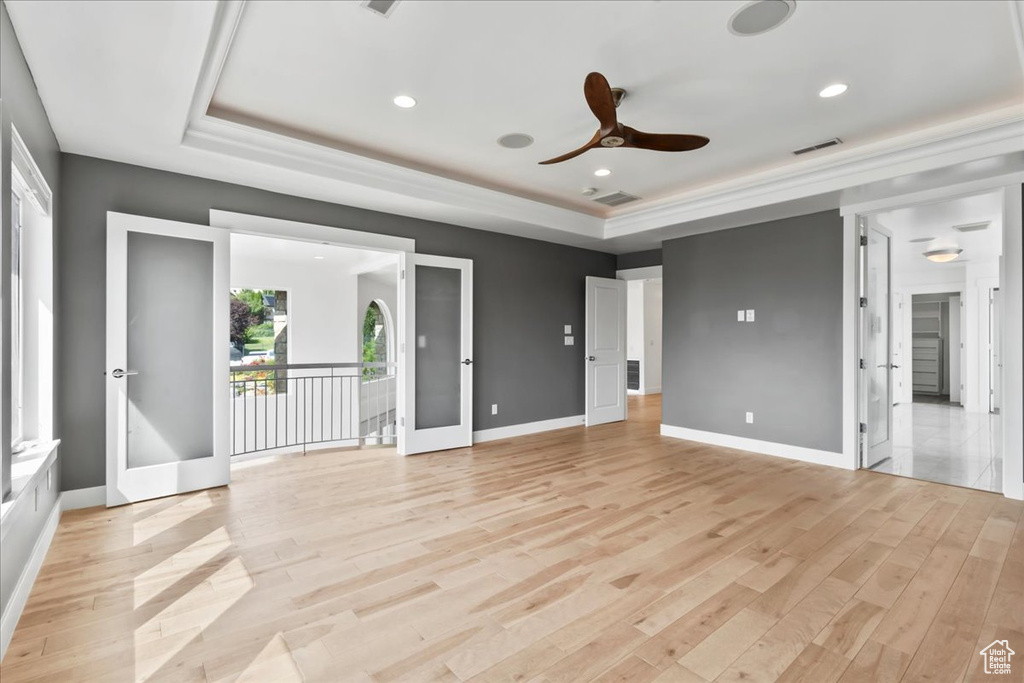 Unfurnished bedroom with ceiling fan, light wood-type flooring, a tray ceiling, and access to outside