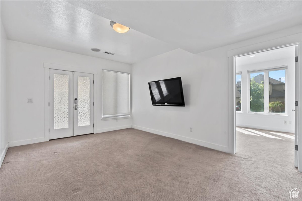 Unfurnished living room with light carpet, french doors, and a textured ceiling