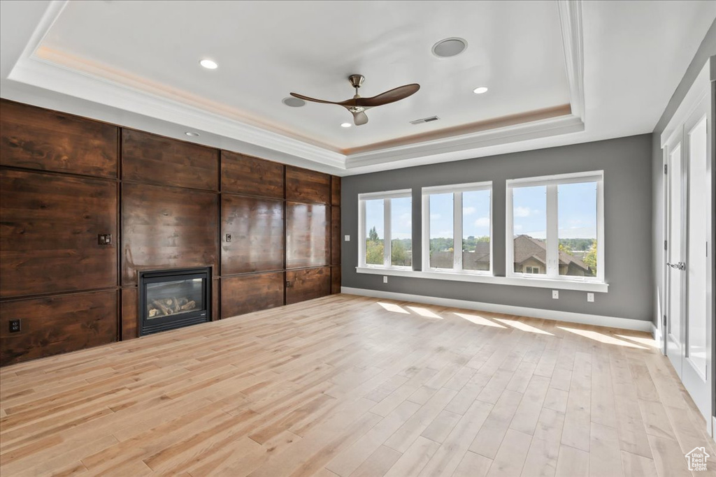 Unfurnished living room with a tray ceiling, ceiling fan, and light hardwood / wood-style floors