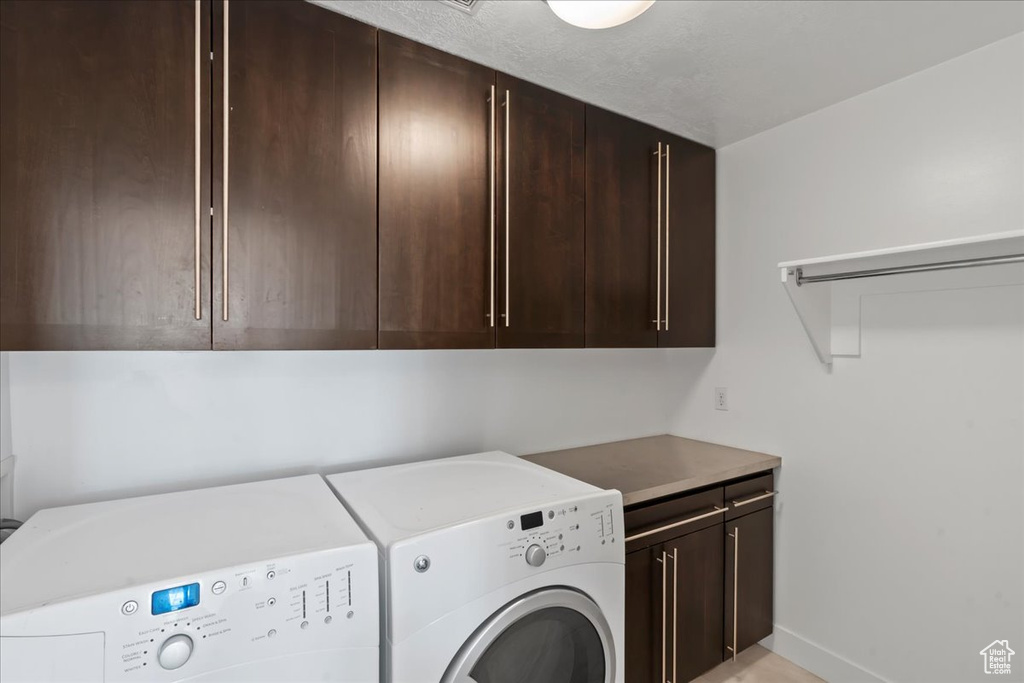 Laundry area with a textured ceiling, cabinets, and washer and clothes dryer