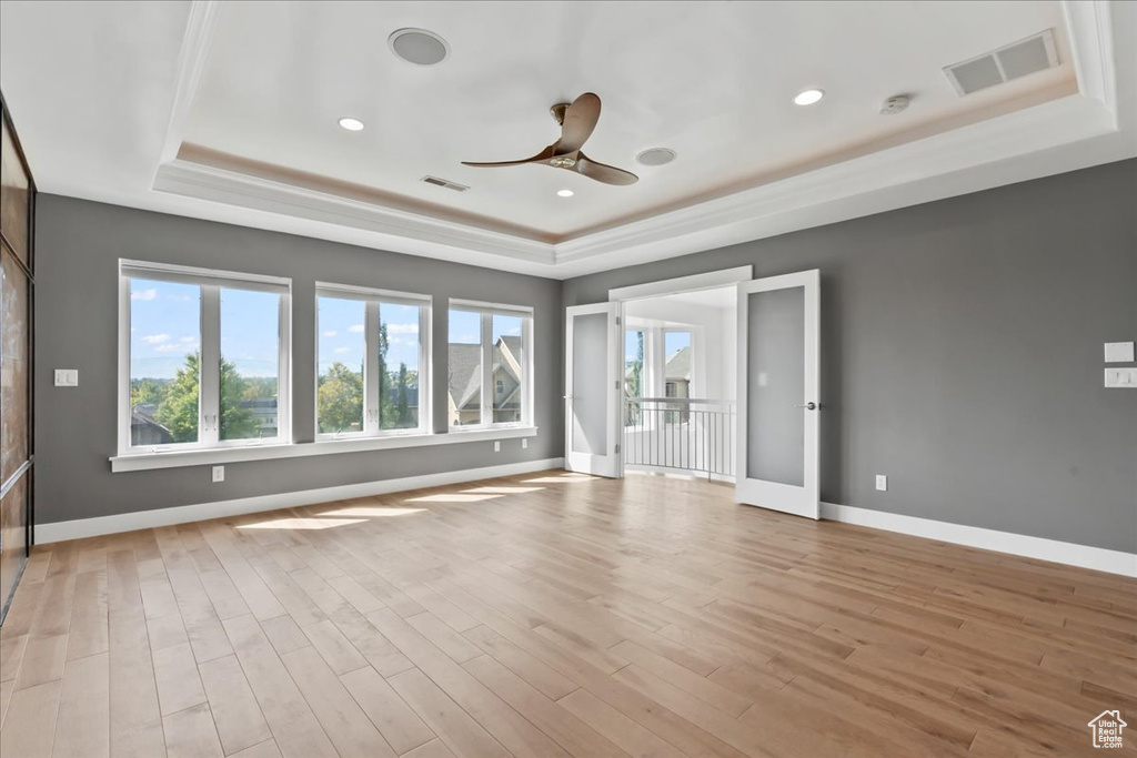 Spare room with a raised ceiling, ceiling fan, and light hardwood / wood-style floors