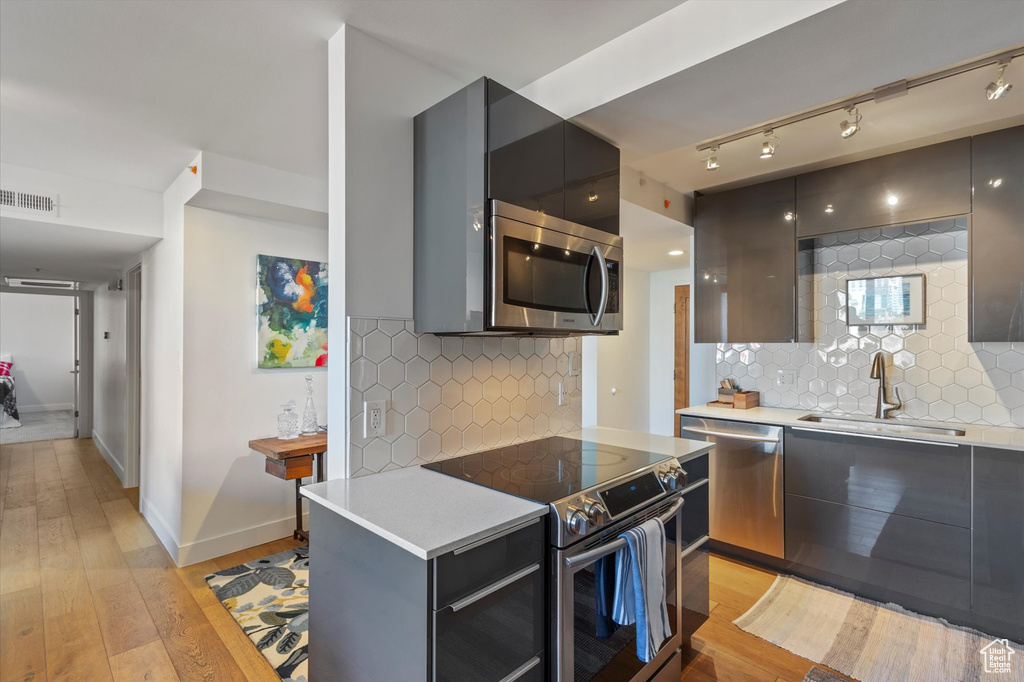 Kitchen with backsplash, light wood-type flooring, sink, and appliances with stainless steel finishes