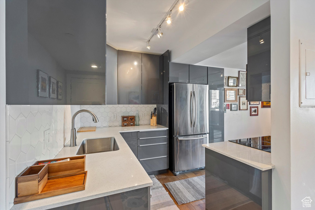 Kitchen with light wood-type flooring, stainless steel refrigerator, sink, gray cabinets, and decorative backsplash