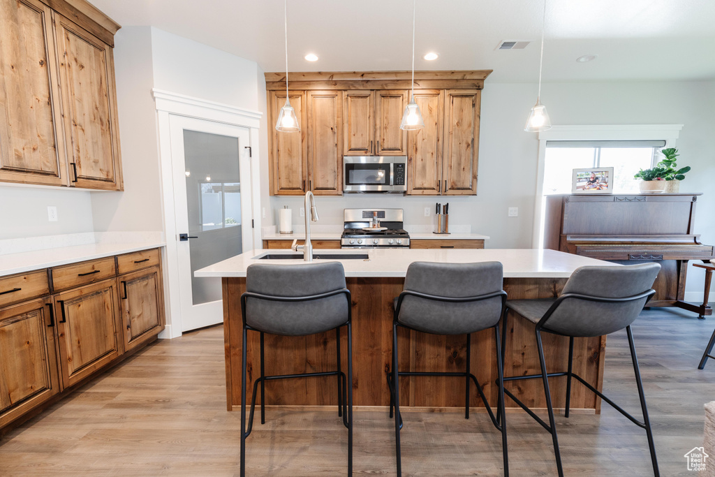 Kitchen featuring an island with sink, hanging light fixtures, stainless steel appliances, sink, and light wood-type flooring