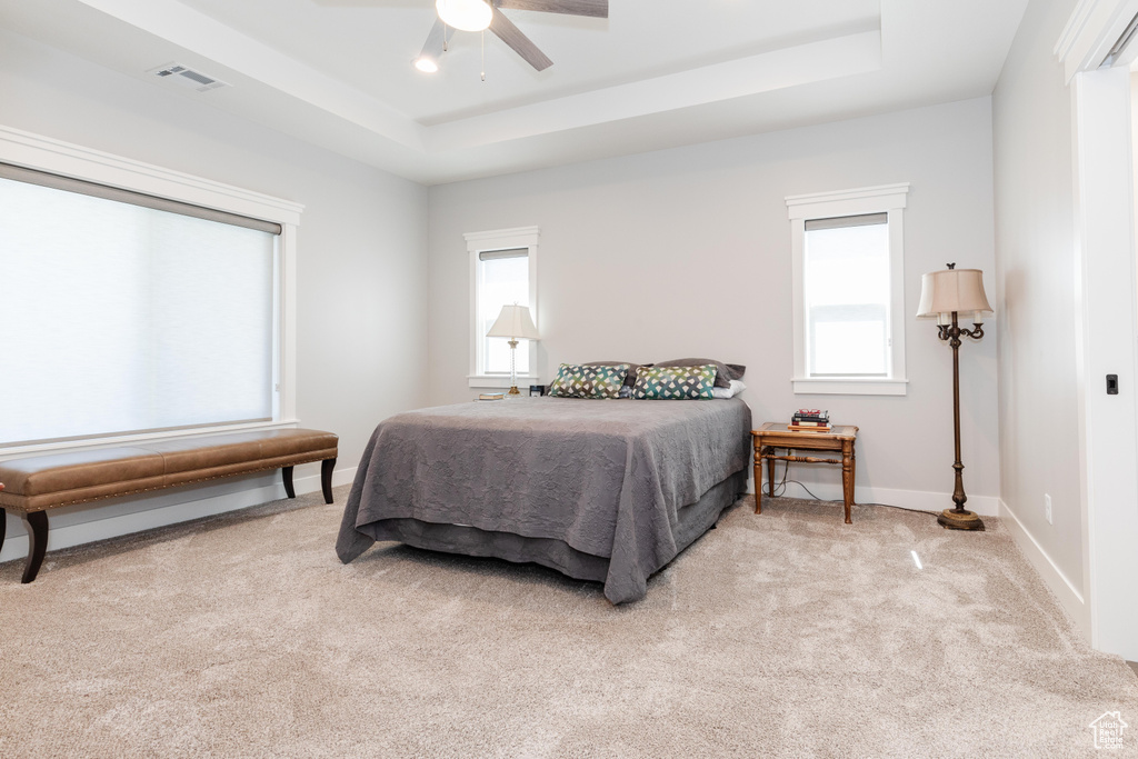 Bedroom with light carpet, a raised ceiling, and ceiling fan