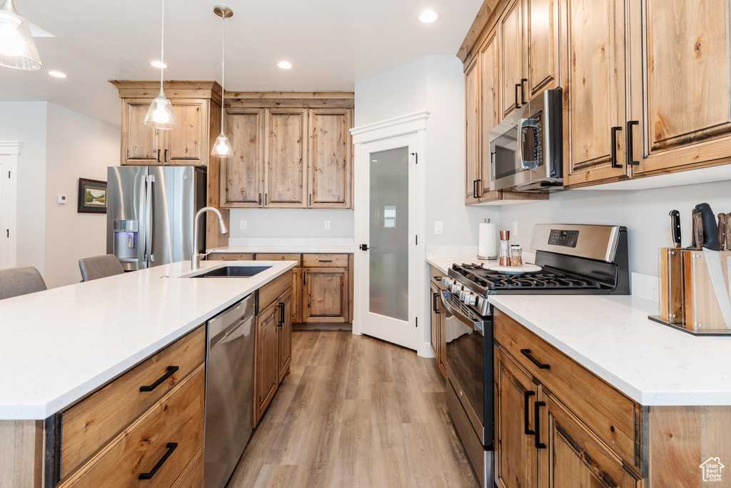 Kitchen featuring a kitchen island with sink, light wood-type flooring, decorative light fixtures, stainless steel appliances, and sink