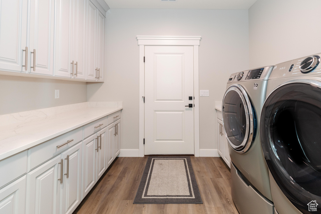 Clothes washing area with washing machine and dryer, cabinets, and light hardwood / wood-style flooring