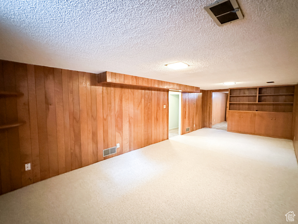 Basement featuring a textured ceiling, carpet flooring, and wooden walls