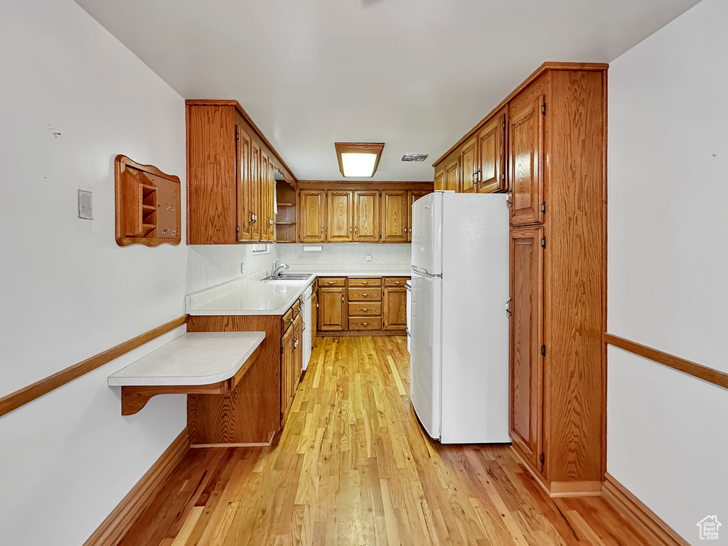 Kitchen with a kitchen bar, white fridge, sink, and light wood-type flooring