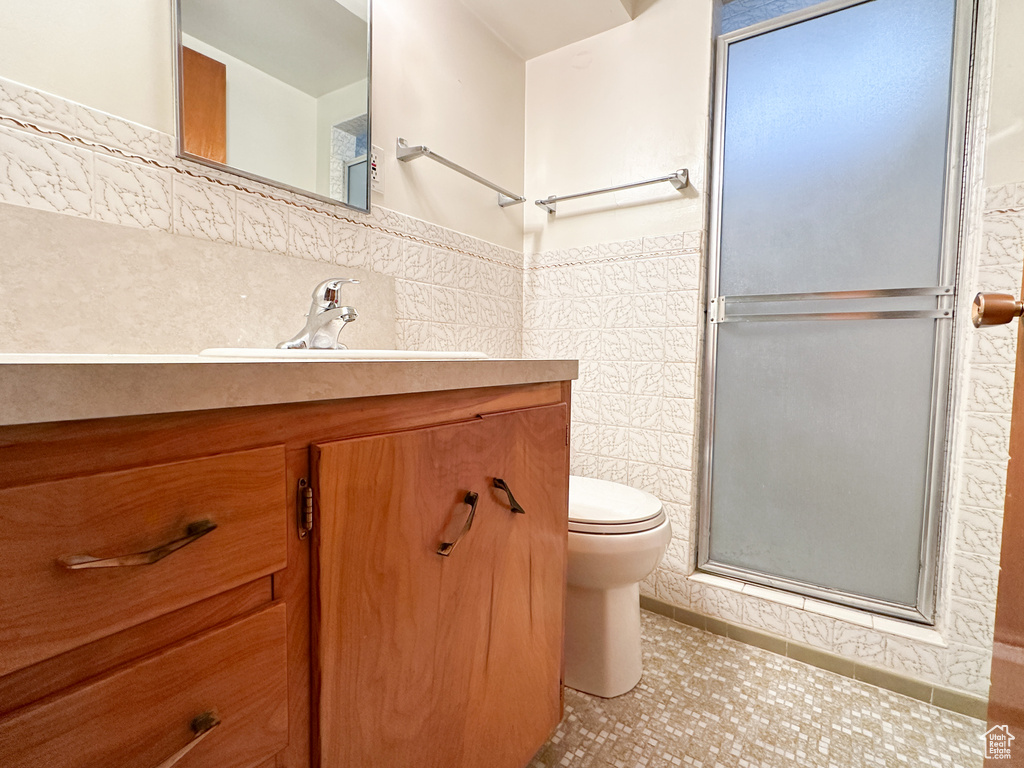 Bathroom featuring toilet, tile patterned flooring, a shower with door, vanity, and tile walls