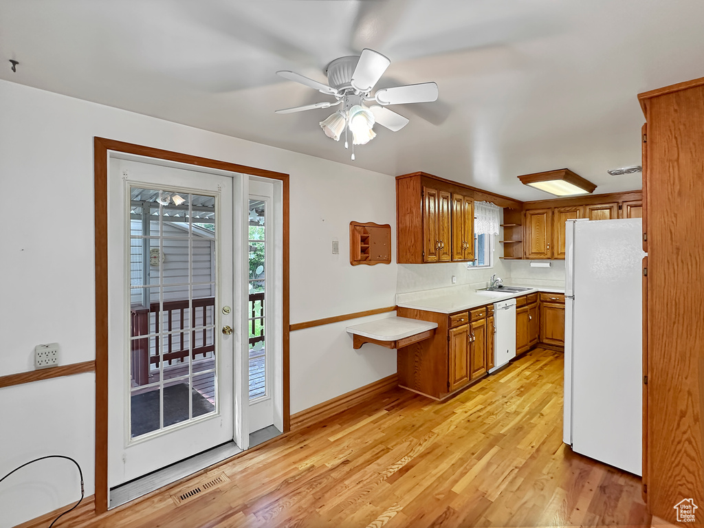 Kitchen with ceiling fan, sink, white appliances, and light hardwood / wood-style floors