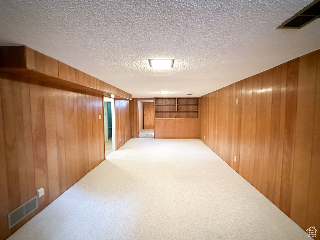 Carpeted empty room featuring a textured ceiling and wooden walls