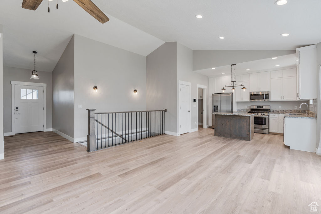 Kitchen featuring stainless steel appliances, a kitchen island, sink, light stone countertops, and ceiling fan