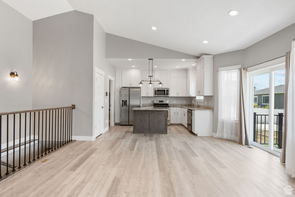 Kitchen featuring vaulted ceiling, decorative light fixtures, appliances with stainless steel finishes, light stone countertops, and a kitchen island