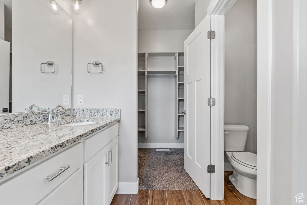 Bathroom with a textured ceiling, vanity, toilet, and wood-type flooring