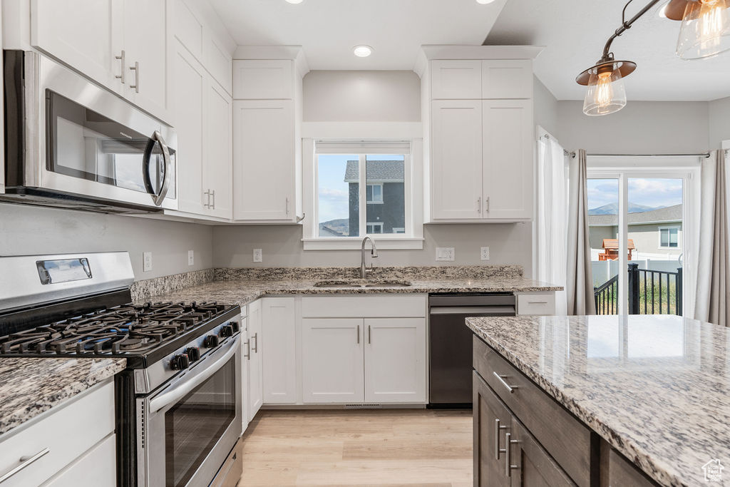 Kitchen with light wood-type flooring, pendant lighting, stainless steel appliances, sink, and white cabinets