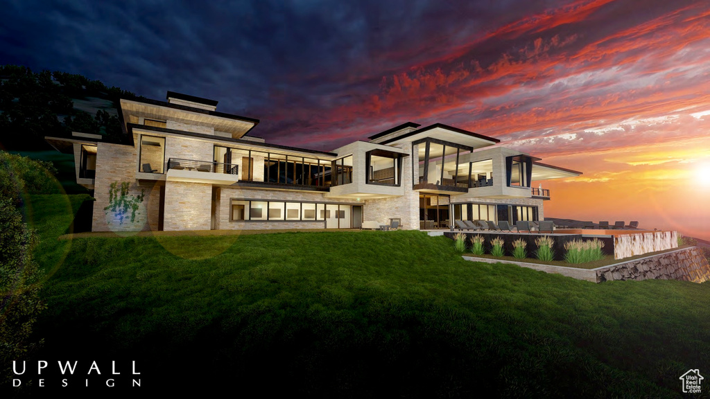 Back house at dusk featuring a balcony and a yard