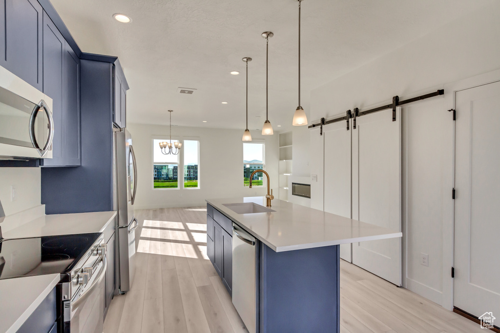 Kitchen with light wood-type flooring, stainless steel appliances, a center island with sink, and a barn door