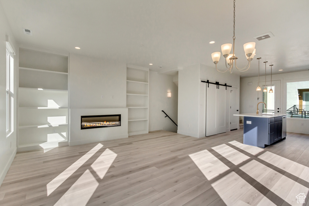 Unfurnished living room featuring a barn door, built in features, a chandelier, and light hardwood / wood-style flooring