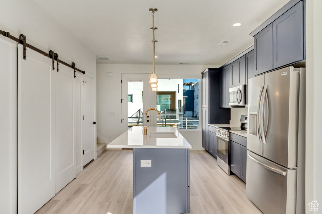 Kitchen featuring a center island with sink, a barn door, stainless steel appliances, and light wood-type flooring