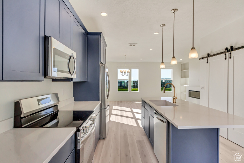 Kitchen with pendant lighting, stainless steel appliances, an island with sink, sink, and a barn door