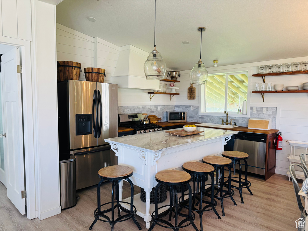 Kitchen with appliances with stainless steel finishes, open shelves, a center island, and light wood finished floors
