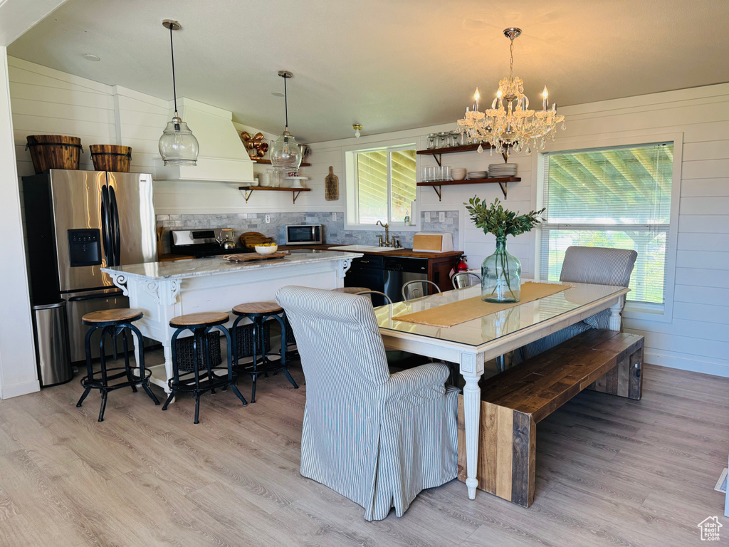 Dining room with light wood-type flooring, a chandelier, plenty of natural light, and wood walls