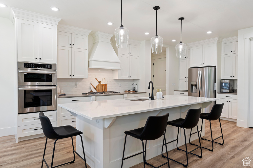 Kitchen with appliances with stainless steel finishes, custom range hood, an island with sink, and sink