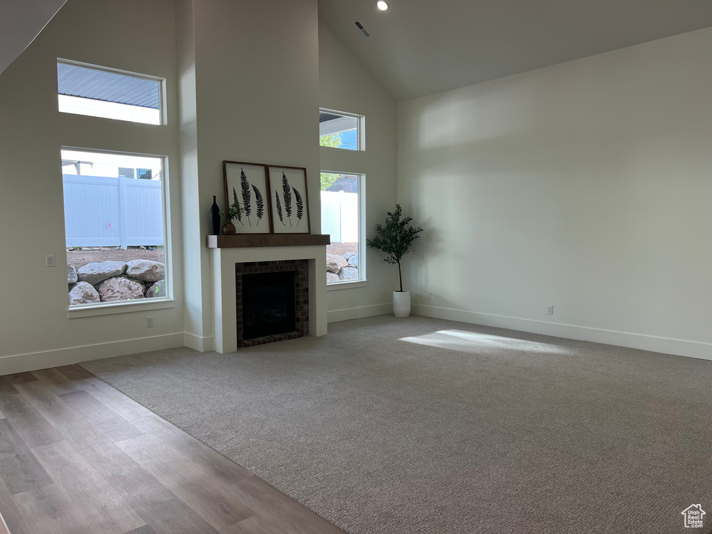 Unfurnished living room featuring visible vents, a brick fireplace, wood finished floors, high vaulted ceiling, and baseboards