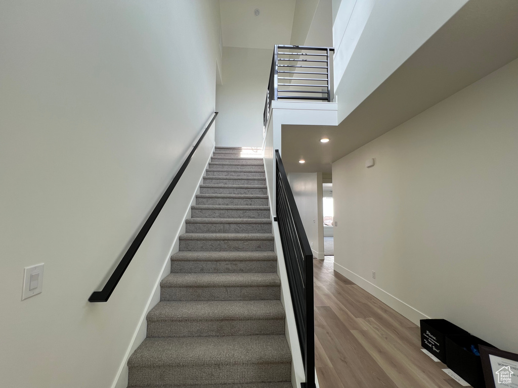Staircase with recessed lighting, baseboards, wood finished floors, and a high ceiling