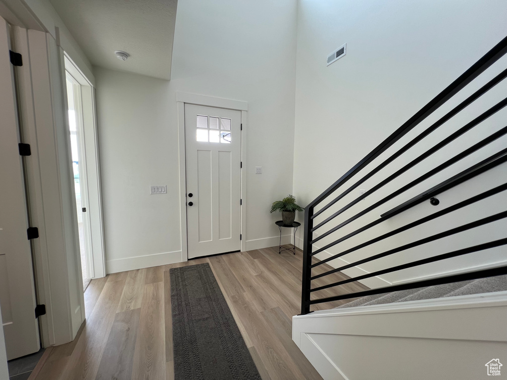 Foyer featuring baseboards, wood finished floors, a towering ceiling, visible vents, and stairway