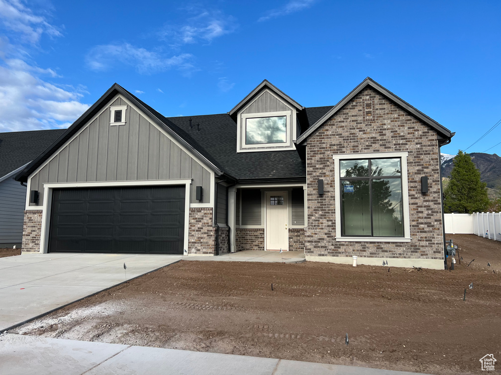 View of front facade with a garage, brick siding, a shingled roof, board and batten siding, and concrete driveway