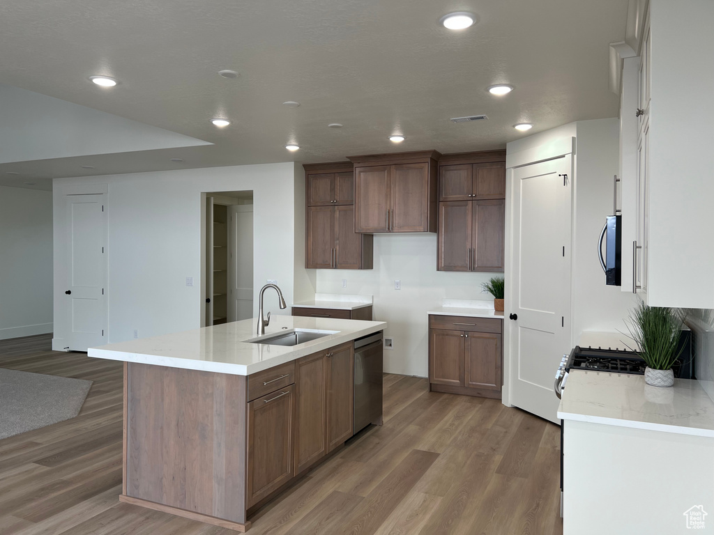 Kitchen featuring stainless steel dishwasher, an island with sink, a sink, and light wood-type flooring