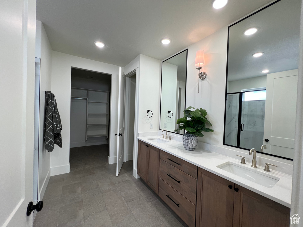 Full bathroom with double vanity, recessed lighting, a spacious closet, a shower stall, and a sink
