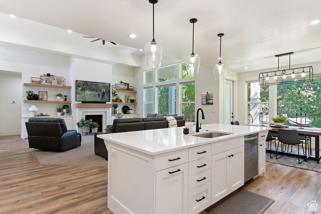 Kitchen featuring light hardwood / wood-style flooring, pendant lighting, an island with sink, sink, and white cabinetry