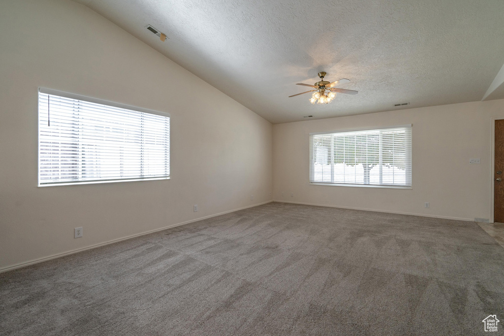 Spare room with a textured ceiling, lofted ceiling, ceiling fan, and carpet flooring