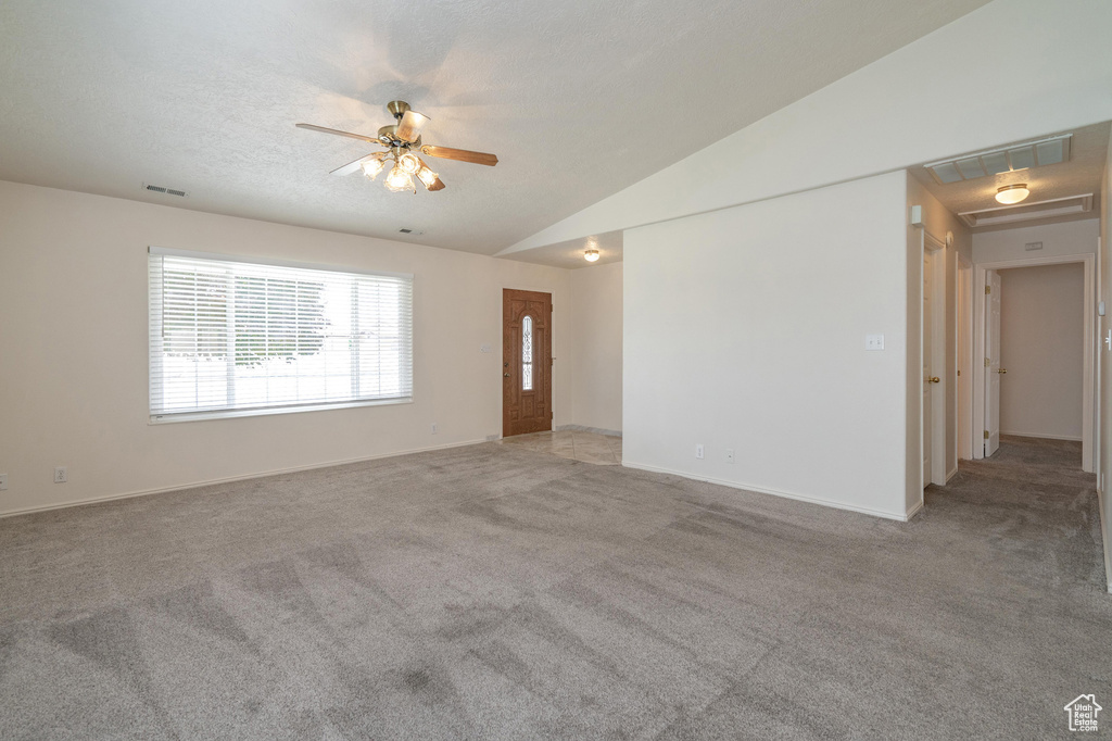 Empty room featuring lofted ceiling, ceiling fan, light carpet, and a textured ceiling