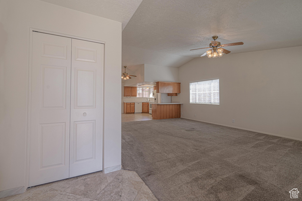 Interior space with a textured ceiling, light colored carpet, ceiling fan, and vaulted ceiling