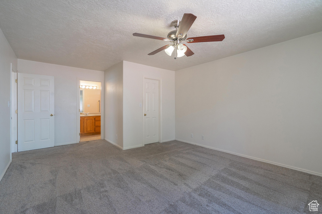 Unfurnished bedroom with a textured ceiling, ensuite bath, carpet, ceiling fan, and a closet