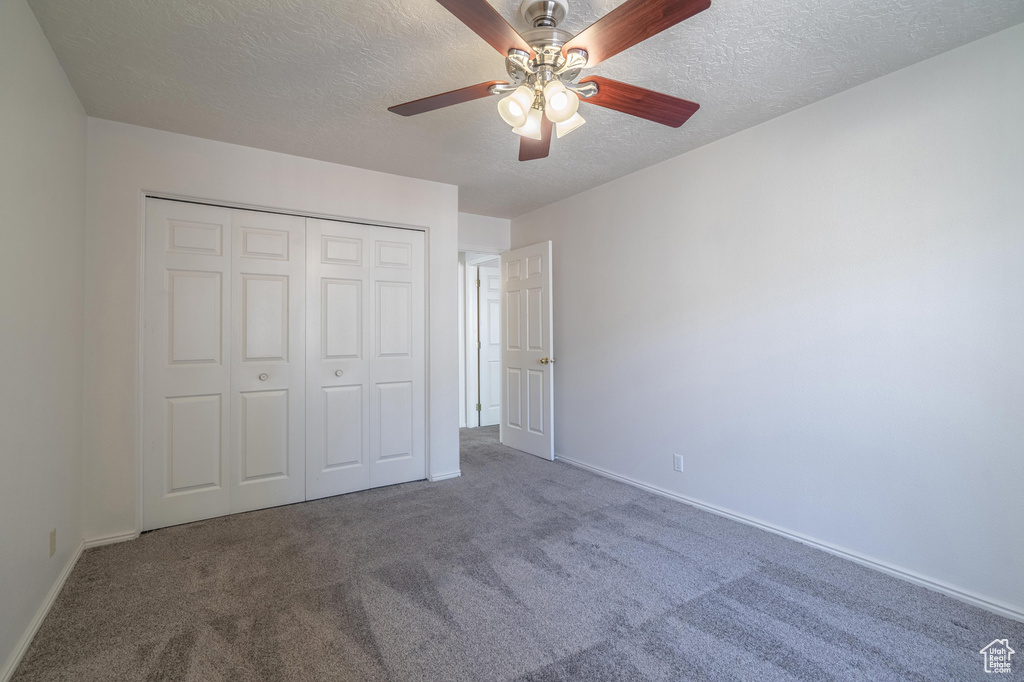 Unfurnished bedroom with a closet, ceiling fan, carpet, and a textured ceiling