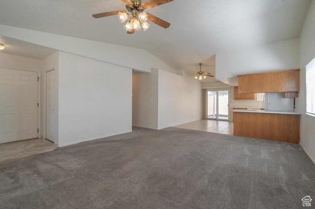 Unfurnished living room featuring ceiling fan, light carpet, and vaulted ceiling