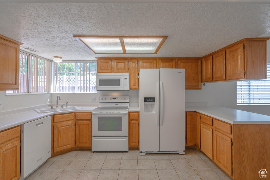 Kitchen with a textured ceiling, sink, white appliances, and light tile patterned flooring