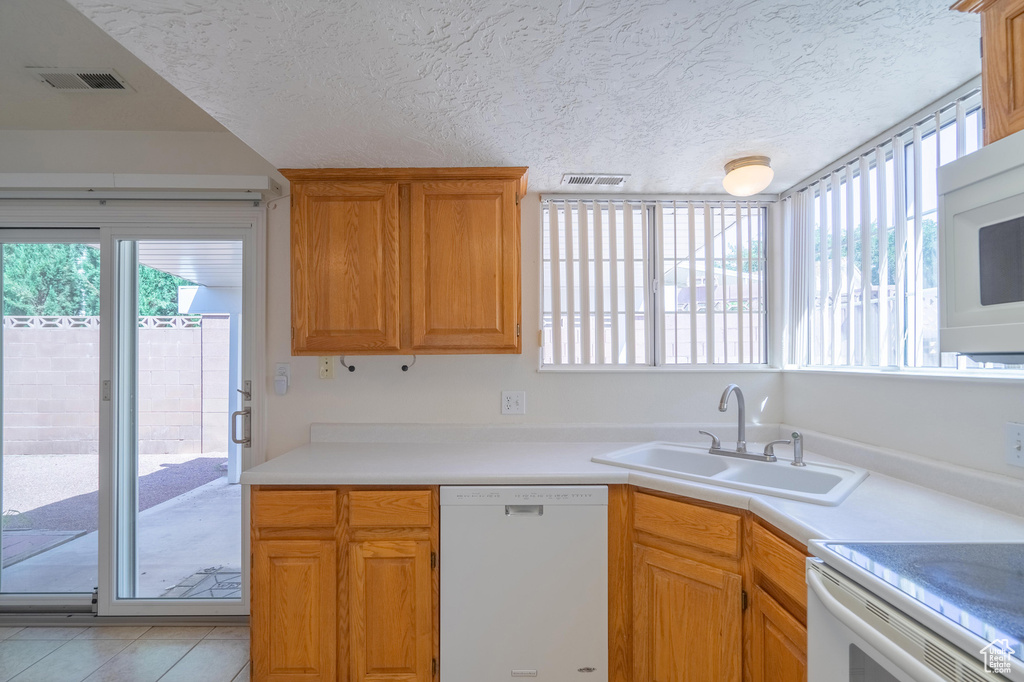 Kitchen with white appliances, light tile patterned floors, a textured ceiling, and sink