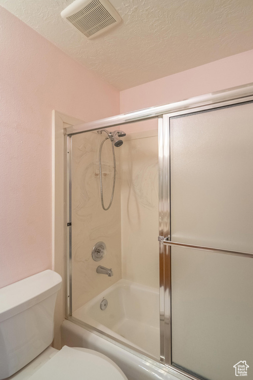 Bathroom featuring a textured ceiling, toilet, and combined bath / shower with glass door