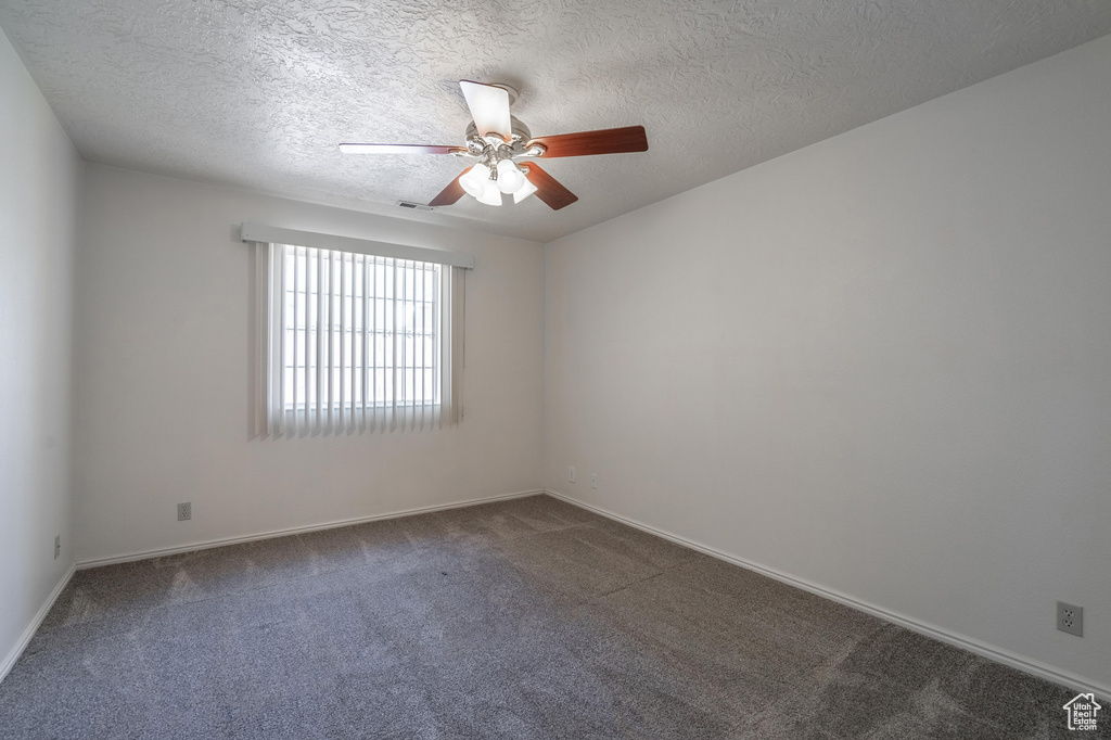 Spare room featuring a textured ceiling, dark colored carpet, and ceiling fan