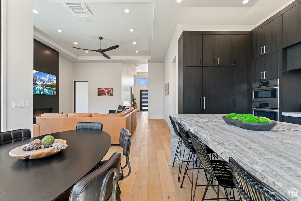 Dining area with a tray ceiling, ceiling fan, plenty of natural light, and light hardwood / wood-style flooring