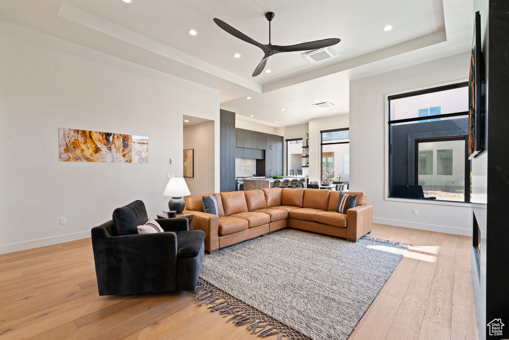 Living room with a tray ceiling, light hardwood / wood-style flooring, and ceiling fan