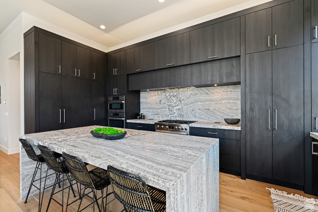 Kitchen featuring backsplash, a kitchen bar, light hardwood / wood-style flooring, appliances with stainless steel finishes, and a kitchen island