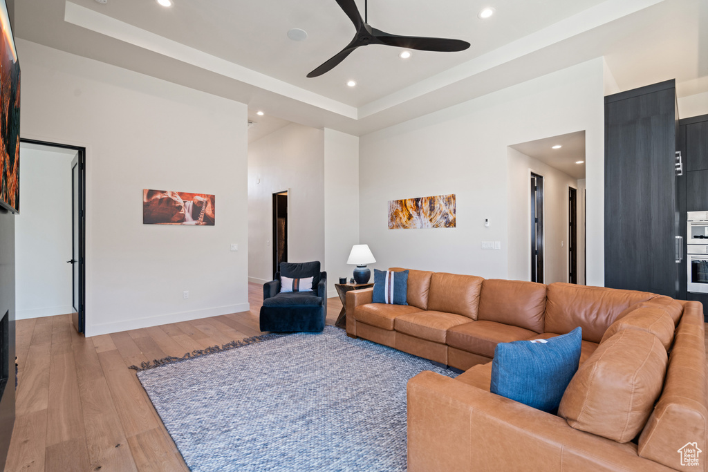 Living room with ceiling fan, a raised ceiling, and light hardwood / wood-style flooring