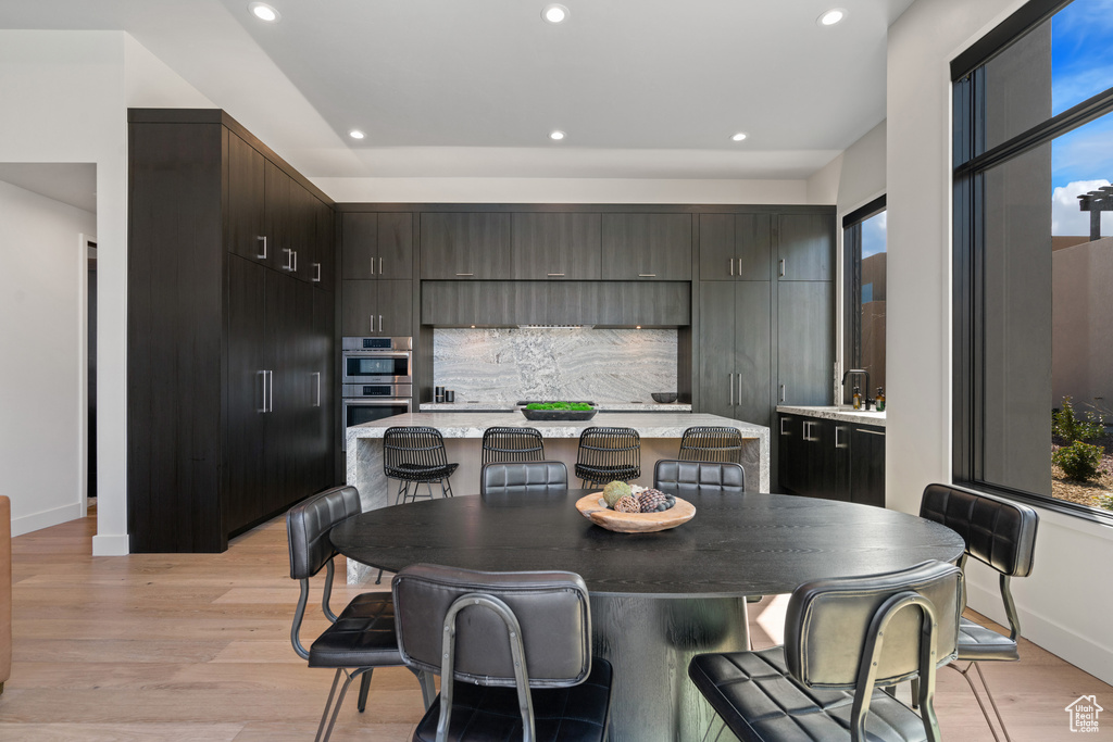 Kitchen featuring light hardwood / wood-style floors, a kitchen bar, a center island, dark brown cabinetry, and double oven